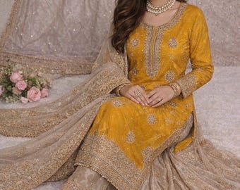 May include: Mustard yellow embroidered salwar kameez with matching dupatta. The outfit features intricate gold embroidery on the neckline, sleeves, and hem. The ensemble includes matching gold embellished pants and gold flats. The background is a neutral color.