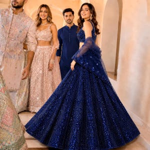 Puede incluir: Un lehenga choli azul profundo con un corpiño sin mangas y una falda voluminosa hasta el suelo, ambos decorados con intrincadas lentejuelas y cuentas tonales, junto con una dupatta transparente a juego drapeada sobre los brazos.