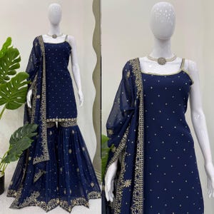 Pu&ograve; includere: Un completo Sharara blu navy esposto su un manichino. L'outfit include un top senza maniche, pantaloni a gamba larga e una sciarpa trasparente. L'ensemble &egrave; adornato da ricami dorati e piccoli abbellimenti sparsi.