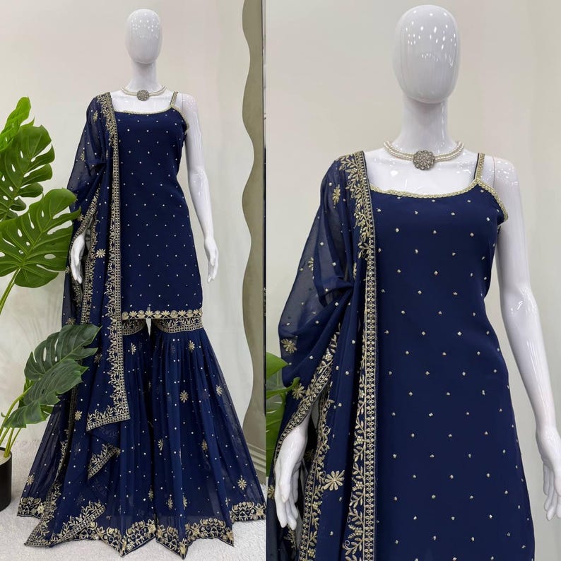 Pu&ograve; includere: Un completo Sharara blu navy esposto su un manichino. L'outfit include un top senza maniche, pantaloni a gamba larga e una sciarpa trasparente. L'ensemble &egrave; adornato da ricami dorati e piccoli abbellimenti sparsi.