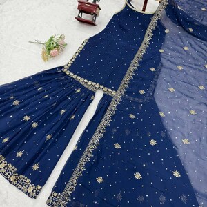 Pu&ograve; includere: Un completo salwar kameez indiano blu navy con ricami e abbellimenti dorati. Il set include un top senza maniche, pantaloni svasati e un dupatta trasparente. Il tessuto &egrave; decorato con piccoli disegni floreali dorati sparsi.