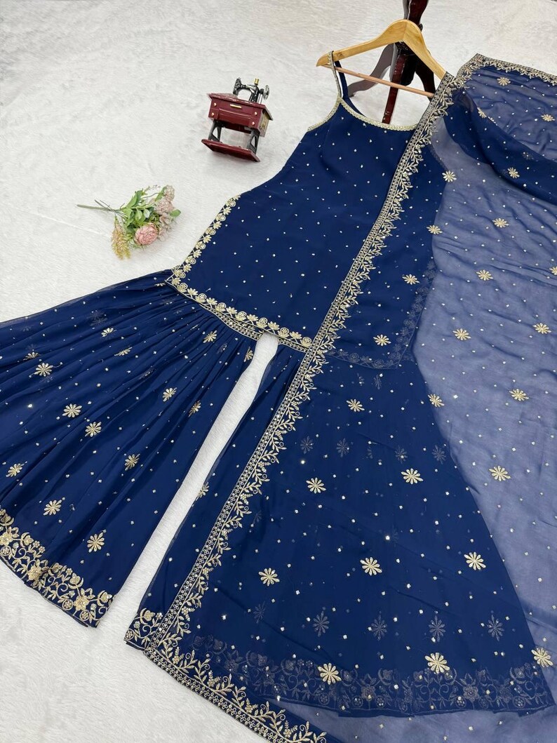 Pu&ograve; includere: Un completo salwar kameez indiano blu navy con ricami e abbellimenti dorati. Il set include un top senza maniche, pantaloni svasati e un dupatta trasparente. Il tessuto &egrave; decorato con piccoli disegni floreali dorati sparsi.