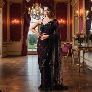 May include: A dark burgundy saree with detailed sequin embellishments. The sleeveless saree has a plunging neckline and a sheer, decorated overlay. The garment is worn in a formal setting with a chandelier and ornate decor.