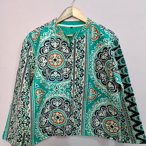 Può includere: Giacca fantasia turchese, bianca, nera e marrone con collo alla coreana e maniche lunghe. La giacca è realizzata in tessuto trapuntato e ha una chiusura con cerniera. Il motivo presenta disegni floreali e geometrici.