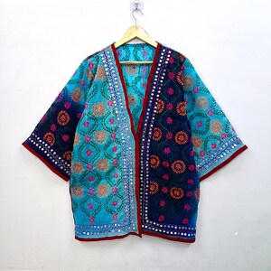Könnte beinhalten: Eine Jacke im Kimono-Stil mit einem zweifarbigen Design in hellem Türkis und tiefem Marineblau. Das Kleidungsstück ist mit aufwendigen Blumenstickereien in Orange und Pink verziert, die durch Reihen kleiner reflektierender Spiegel an den Kanten betont werden.