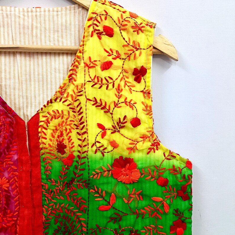 May include: A sleeveless vest featuring a vibrant gradient of yellow and green fabric with intricate red floral and vine embroidery. The garment has a V-neckline and a light beige and white pinstriped lining visible on the interior side.