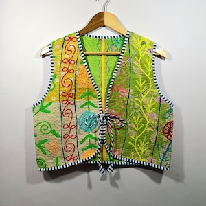 May include: A colorful, sleeveless vest with a unique patchwork design. The vest features a variety of embroidered patterns in shades of green, yellow, orange, and red. It has a striped trim and a tie closure at the front.