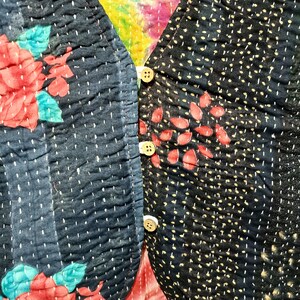 Op de afbeelding: Close-up van een gewatteerd textiel met een bloemmotief. De stof is donkerblauw met rode bloemen en blauwgroene bladeren. De rechterkant heeft een stippenpatroon met rode bladvormen en drie witte knopen.