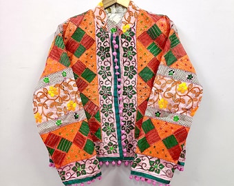 May include: A long-sleeve jacket featuring a patchwork design of orange and green squares, accented with floral embroidery in yellow and green. The front closure includes a row of small pink pom-poms, with additional pink pom-poms along the hem.