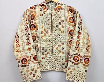 May include: A cream-colored jacket featuring intricate embroidery in shades of orange, brown, and gold. The garment is adorned with small circular mirrors throughout the front panels and sleeves, arranged in geometric and floral patterns.