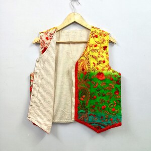 May include: A sleeveless vest featuring a vibrant yellow-to-green gradient on the front panel with intricate red floral embroidery. The interior and back panel consist of a light beige fabric with thin vertical brown stripes and a red trim.