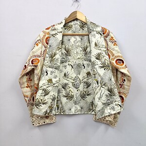 May include: A long-sleeve jacket featuring an off-white base with a detailed black and white jungle print interior showing monkeys, tigers, and birds. The exterior sleeves and shoulders display orange and brown floral embroidery with small mirrors.