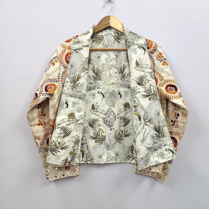 May include: A long-sleeve jacket featuring an off-white base with a detailed black and white jungle print interior showing monkeys, tigers, and birds. The exterior sleeves and shoulders display orange and brown floral embroidery with small mirrors.