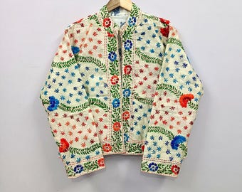May include: A cream-colored quilted jacket featuring an all-over pattern of embroidered red, blue, and green floral motifs and leafy vines. The garment has long sleeves, a straight hem, and a central front opening, all finished with stitching.