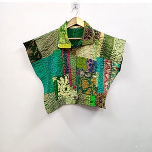 May include: A short-sleeved button-down shirt featuring a patchwork design in various shades of green. The garment is constructed from multiple fabric panels with intricate stitching patterns, a classic collar, and a front button closure.