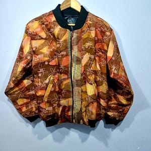 May include: A patterned bomber jacket with a brown, orange, and yellow floral design. The jacket has a black collar, cuffs, and hem, and a full-length zipper. The fabric has a shiny appearance.