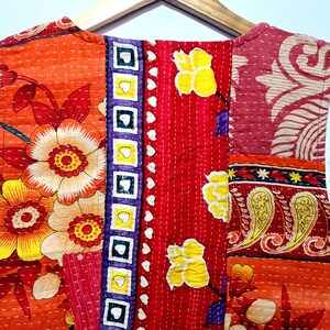 Op de afbeelding: Een patchwork kledingstuk met een levendige mix van kleuren en patronen. Het ontwerp bevat grote bloemmotieven in oranje, geel en wit, naast geometrische en paisley-elementen. Het kledingstuk is aan elkaar gestikt met zichtbaar wit garen.
