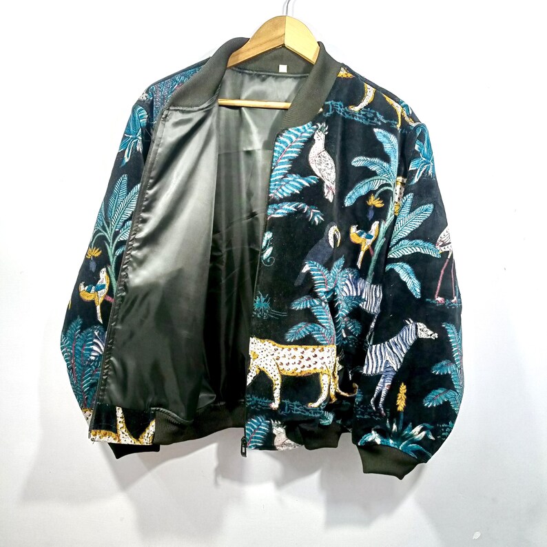 May include: Black bomber jacket with a vibrant jungle-themed print. The design features zebras, leopards, parrots, and lush foliage in shades of teal, yellow, and white. The jacket has a satin lining and a zip-up front.