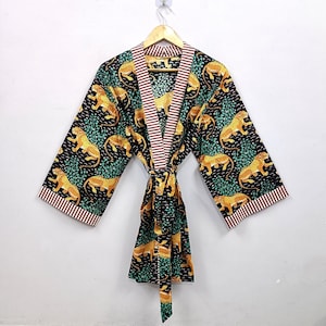 Könnte beinhalten: Ein schwarzer Kimono-Bademantel mit einem sich wiederholenden Muster aus gelben und schwarzen Leoparden inmitten von grünem Blattwerk. Das Kleidungsstück hat weite Ärmel und eine mit braun-weiß gestreifte Kante versehene Vorderseite sowie einen Bindegürtel.