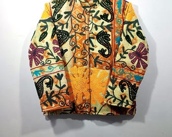 May include: A cream-colored jacket with an intricate floral and paisley design in shades of orange, yellow, purple, and black. The jacket has a mandarin collar and a button-up front. The sleeves are long, and the jacket is hanging on a wooden hanger.