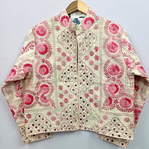 May include: An off-white jacket featuring intricate pink floral embroidery and small circular mirrors. The garment has a mandarin collar, long sleeves, and a front opening, with decorative stitching patterns covering the entire surface.