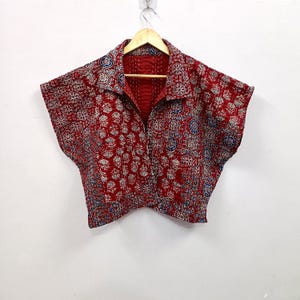 Könnte beinhalten: Eine kurzärmelige, bauchfreie Jacke mit einer leuchtend roten Grundfarbe und komplizierten blauen und weißen Blumen- und Geometriemustern im Blockdruck. Das Kleidungsstück hat einen breiten Kragen, eine Knopfleiste und sichtbare weiße Nähte.