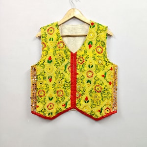May include: A bright yellow sleeveless waistcoat featuring intricate green and red floral embroidery, small circular mirrors, and a red fabric trim along the front opening and bottom hem. The interior lining is a light beige fabric with thin vertical stripes.