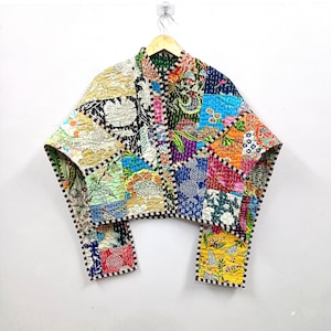 Puede incluir: Una chaqueta corta hecha de tela de patchwork acolchada con una variedad de coloridos patrones florales y geométricos en tonos amarillos, azules, verdes y rojos. La prenda tiene mangas largas, cuello mao y un borde de color marrón y blanco.