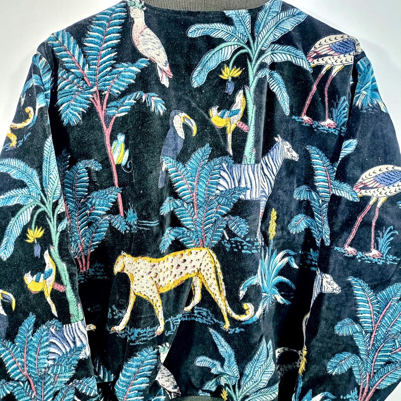 May include: Black jacket with a vibrant jungle-themed design. The pattern includes blue palm trees, a zebra, a cheetah, and various birds. The jacket has a dark green collar and cuffs.