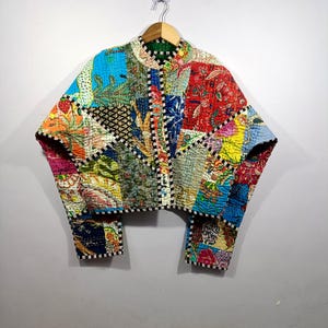 May include: A colorful patchwork jacket with a variety of floral and geometric patterns. The jacket features a round collar, long sleeves, and a cropped length. The jacket is made of quilted fabric and has a black and white striped trim.