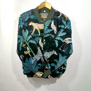 May include: Black bomber jacket with a jungle-themed pattern. The jacket features a repeating design of zebras, leopards, birds, and tropical plants in shades of teal, yellow, and white. The jacket has a green collar, cuffs, and hem.