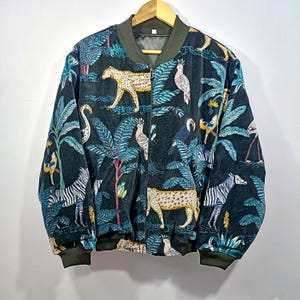 Handmade velvet bomber jacket with dark teal and navy base, featuring jungle-inspired animal and bird illustrations including leopards, zebras, and tropical foliage.