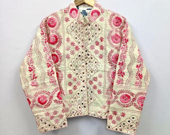 May include: A cream-colored jacket featuring intricate pink floral embroidery and small circular mirror accents. The garment has a mandarin collar, long sleeves, and a button-front closure, with repeating patterns of flowers and geometric shapes.