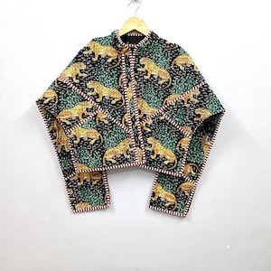 Peut inclure: Une veste matelassée sur fond noir avec un motif répétitif de léopards jaunes et noirs au milieu d'un feuillage vert. Le vêtement possède un col montant, des manches longues et une bordure rayée rouge et blanche sur toutes les coutures.