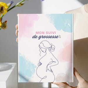 May include: A rectangular book with a white cover featuring a dark blue continuous line drawing of a pregnant person. The background has soft, watercolor-style patches of light pink and light blue. The text reads MON SUIVI de grossesse.
