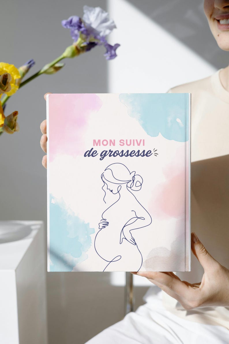 May include: A rectangular book with a white cover featuring a dark blue continuous line drawing of a pregnant person. The background has soft, watercolor-style patches of light pink and light blue. The text reads MON SUIVI de grossesse.