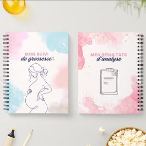 May include: Two spiral-bound notebooks with white covers. The left notebook features a line drawing of a pregnant person and the text "MON SUIVI de grossesse" with blue and pink watercolor accents. The right notebook shows a medical clipboard icon and the text "MES R&Eacute;SULTATS d'analyse" with pink watercolor and gold flecks.
