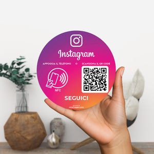 Può includere: Un cartello rotondo di Instagram con uno sfondo sfumato viola, rosa e arancione. Il cartello presenta il logo di Instagram, la parola "Instagram", un codice QR e il testo "Seguici". Il cartello è tenuto in una mano.