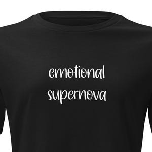 以下が含まれることがあります： 黒いTシャツ。白い筆記体フォントで「emotional supernova」の文字がプリントされています。Tシャツは半袖で、クルーネックです。テキストは前面の中央に配置されています。