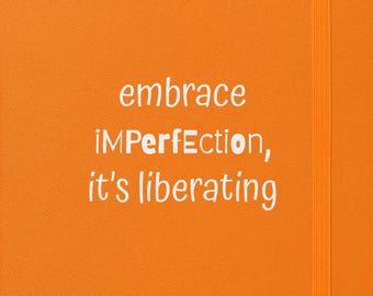 May include: An orange notebook with an elastic band closure. The cover features the white text: "embrace iMPERFECTION, it's liberating". The notebook is closed and has a vertical orientation.