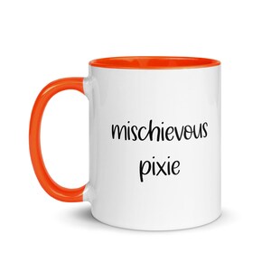 Puede incluir: Taza de cerámica blanca con interior y asa naranja. La taza presenta las palabras "mischievous pixie" en escritura negra. Un diseño sencillo y divertido para una taza de café o té.