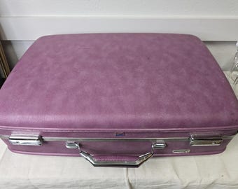 Può includere: Una valigia rettangolare vintage in una tonalità viola tenue. La valigia presenta una superficie strutturata, una maniglia color argento e chiusure in metallo. Il manico è avvolto in materiale viola abbinato. Un classico accessorio da viaggio.
