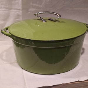 May include: A green enameled cast iron Dutch oven with a matching lid. The pot has a silver handle on the lid and two side handles. The pot is sitting on a white surface.