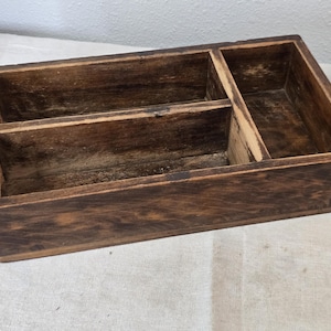 Antiguo utensilio primitivo de madera con tres compartimentos y contenedores de almacenamiento.