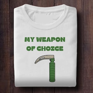 May include: White t-shirt with the text "MY WEAPON OF CHOICE" in green block letters. Below the text is a graphic of a medical laryngoscope in green, silver, and tan.