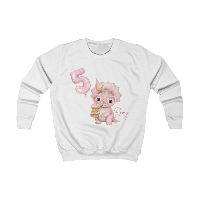 Puede incluir: Sudadera blanca con un dinosaurio rosa sosteniendo una magdalena y un globo rosa con el n&uacute;mero 5. El dinosaurio lleva un gorro de fiesta. El nombre "Romy" est&aacute; escrito en cursiva. Dise&ntilde;o tem&aacute;tico de cumplea&ntilde;os infantil.