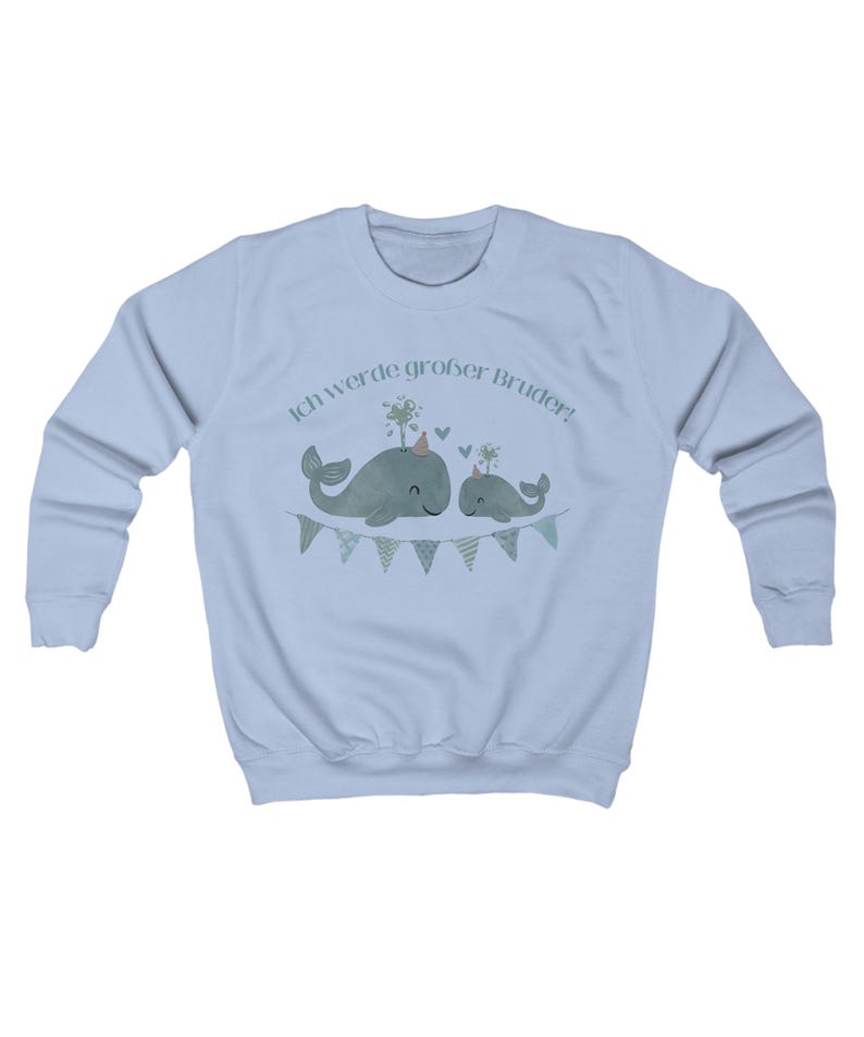 May include: A light blue sweatshirt featuring a graphic of two whales wearing party hats and a banner. The text "Ich werde gro&szlig;er Bruder!" is above the whales. The whales are light green with a light green banner.