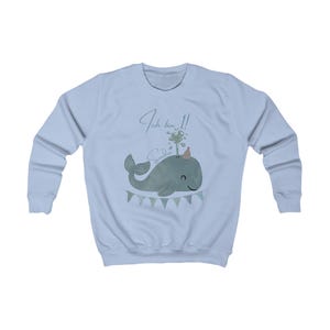May include: Light blue sweatshirt featuring a cartoon whale design. The whale is gray-green and wears a party hat. The text "Ich bin 1!" and the name "Sandie" are above the whale. A banner with triangular flags is below the whale.