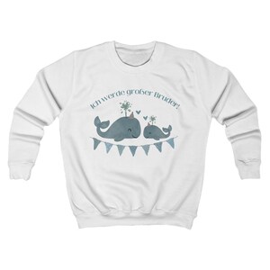 May include: White sweatshirt featuring a blue whale graphic with the text "Ich werde gro&szlig;er Bruder!" above the whales. The whales are decorated with party hats and are above a blue pennant banner. The sweatshirt has long sleeves and a crew neck.