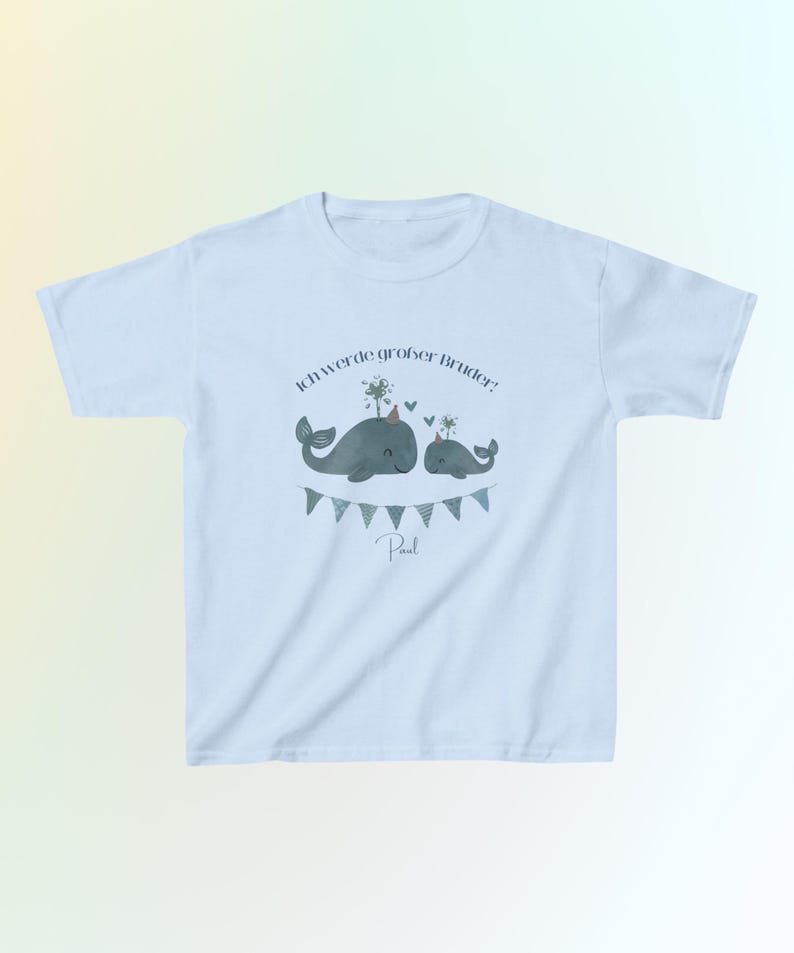 May include: A light blue t-shirt featuring a graphic of two grey whales wearing party hats, with the German text "Ich werde gro&szlig;er Bruder!" above them, a small heart, and a string of blue and grey triangular bunting flags below, with the name "Paul".